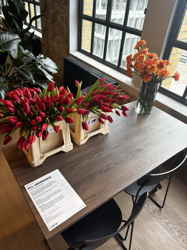 Crates of red tulips and a vase of orange chrysanthemums on a dark wooden table next to a sunlit window