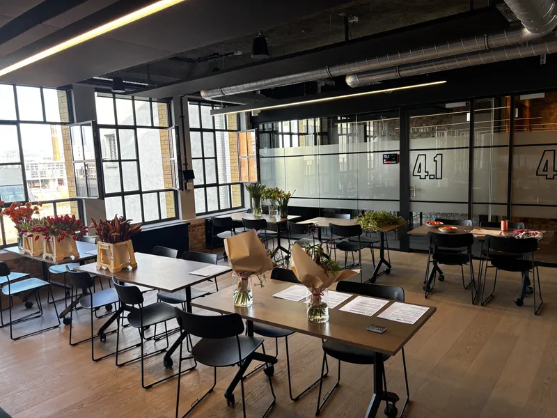An open-plan office set up for flower arranging, with paper-wrapped bouquets and buckets of tulips on long tables by tall windows